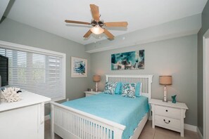 A bedroom with a white bed, a ceiling fan, a window with blinds, and a nightstand with a lamp. - Cassine Station 30A by Panhandle Getaways (Santa Rosa Beach)
