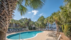 Una piscina con sillas de descanso, rodeada de palmeras y un paseo de ladrillo.