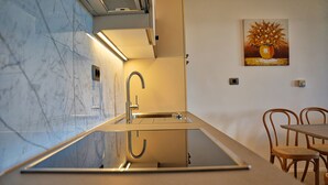 Une cuisine moderne avec un pare-feu en verre, un évier en acier inoxydable et des chaises en bois autour d’une table.