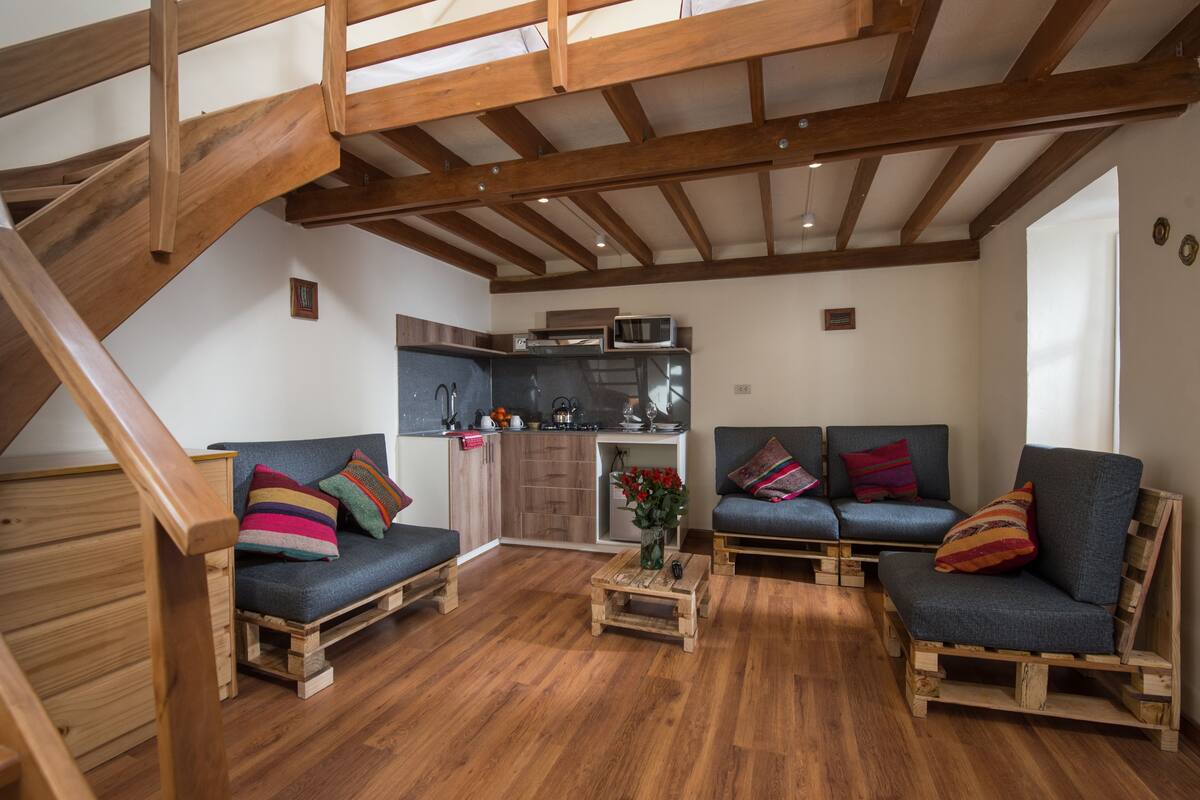 A loft-style living area with wooden beams, a kitchen, and a staircase.