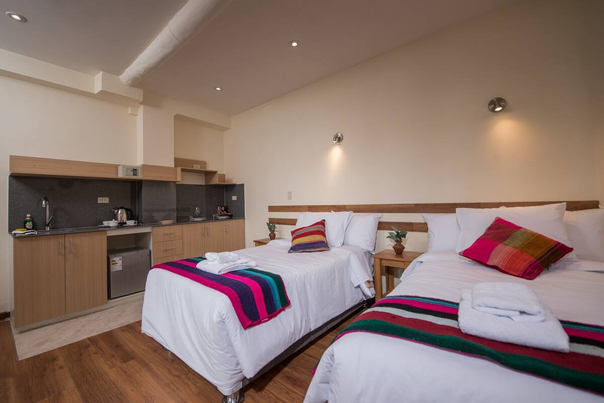 A hotel room with two beds, a kitchenette, and a small bathroom.