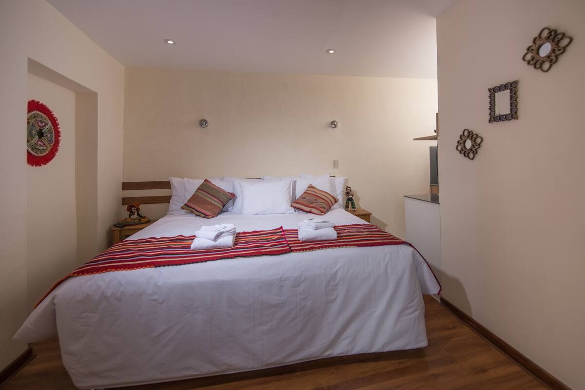 A neatly made bed with white linens and striped blankets, a wooden headboard, and decorative wall art.