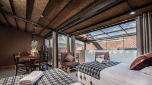 A hotel room with two beds, a dining table, and a chair. The room has a large window with a view of the city. - Casa Cavassa Centro Histórico Cusco (Cusco)
