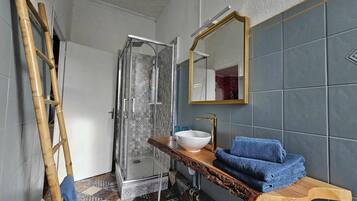 A bathroom with a glass shower enclosure, a white sink with a gold faucet, and a wooden vanity with blue towels.