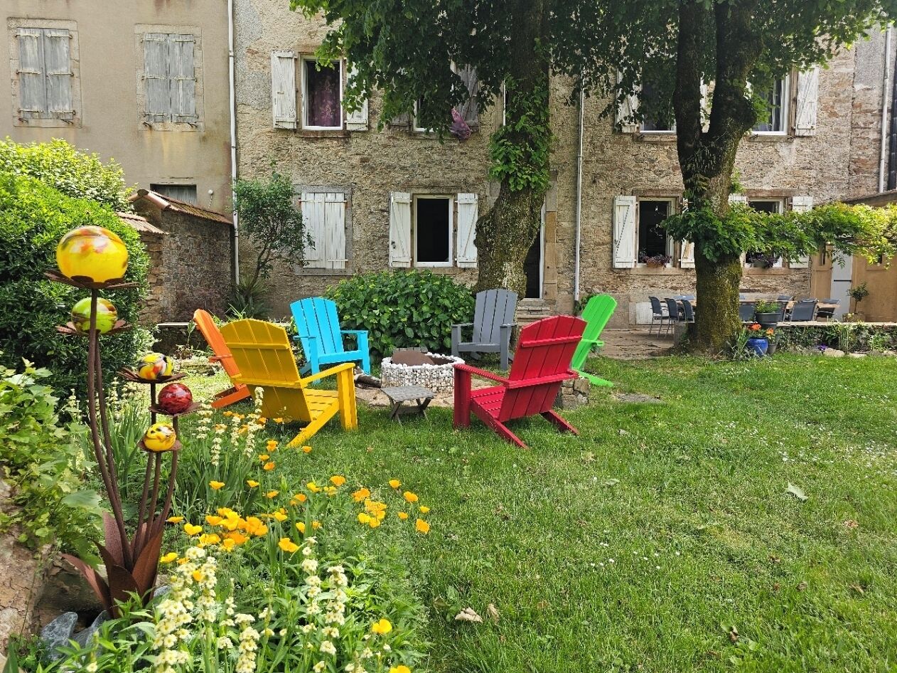 A garden with colorful Adirondack chairs, a small table, and a variety of flowers.