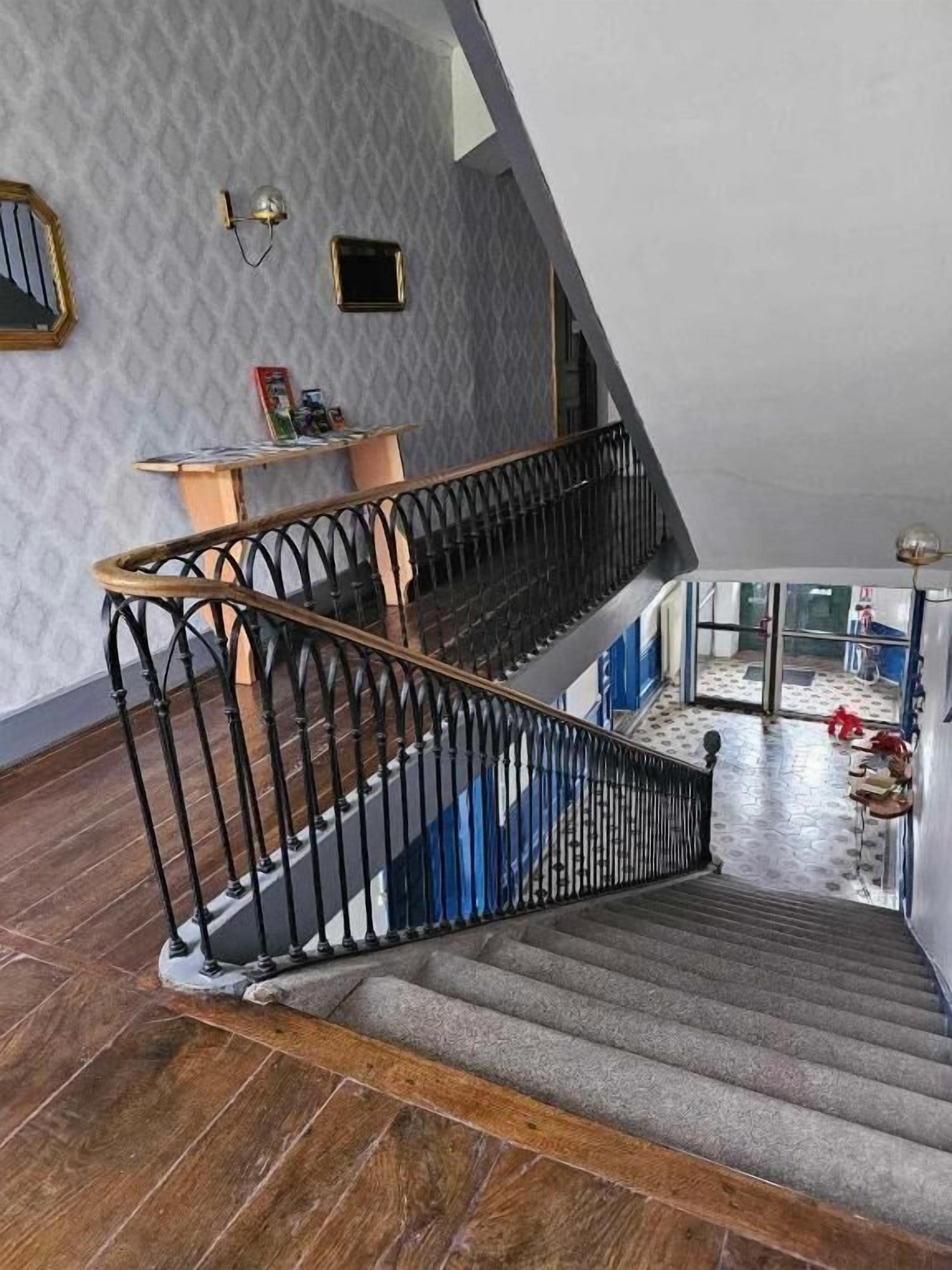 Una escalera con barandilla de madera y balaustradas negras, que conduce a un rellano con una pequeña mesa y un aplique de pared.