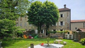 A courtyard with a large tree, outdoor seating, and a stone building with multiple windows.