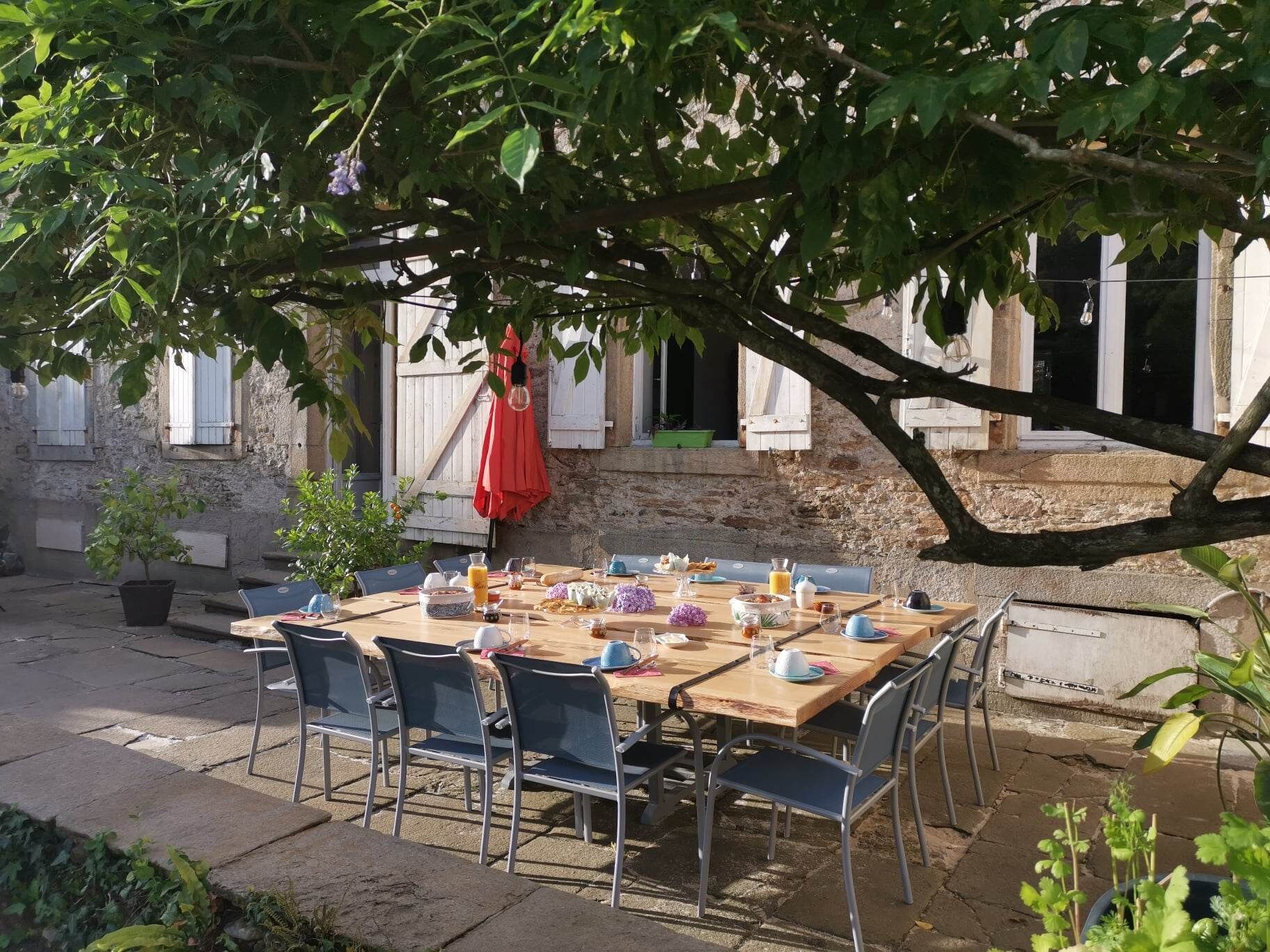 Un espace de restauration en plein air, avec une table en bois et des chaises en métal, adossé à un mur de pierres rustiques.