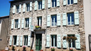 A stone building with multiple windows and shutters, a sign indicating it is a hotel, and potted plants in front.