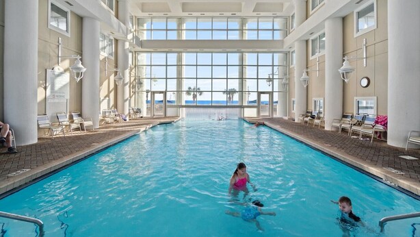An indoor swimming pool with clear views of the ocean, surrounded by lounge chairs and a tiled floor. - Majestic Sun Beach Resort by Panhandle Getaways (Miramar Beach)