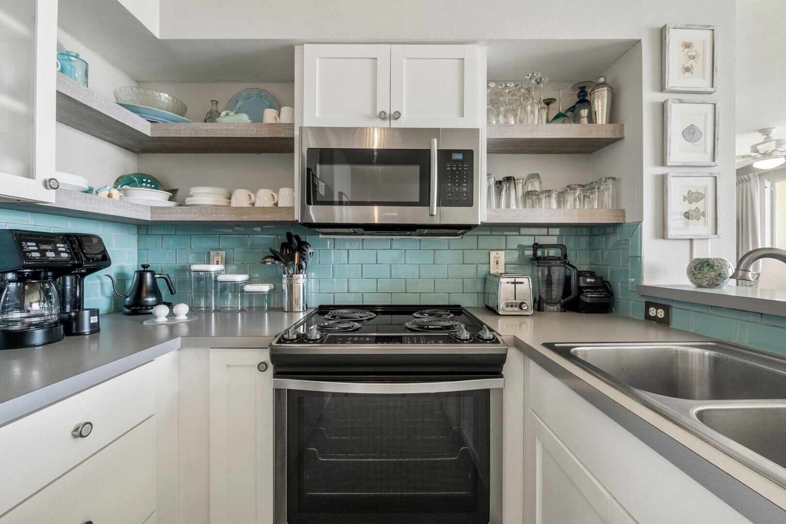 A modern kitchen with white cabinets, a stainless steel microwave, a gas stove, and a built-in oven. There are shelves above the stove holding glassware and a coffee maker on the counter.