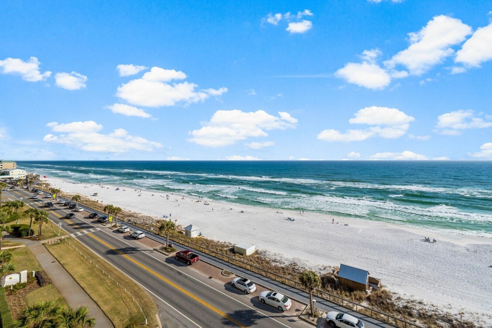 A coastal road with beach access, a parking area, and a view of the ocean.