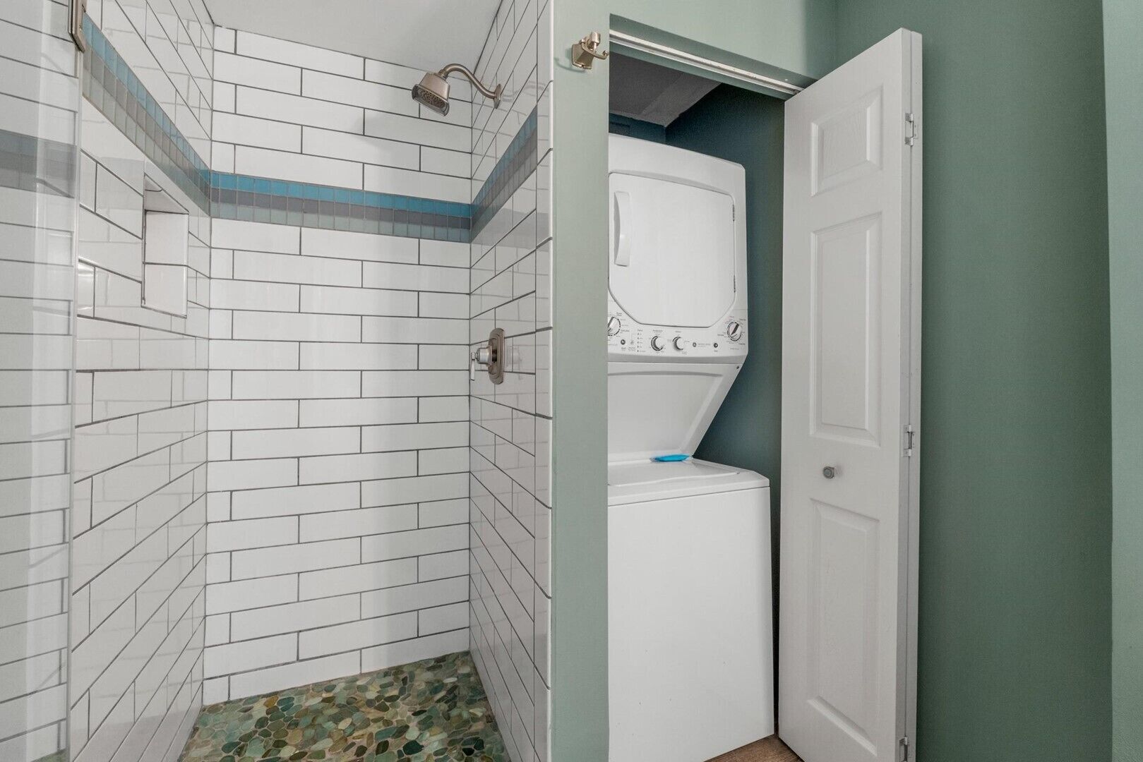 Un baño con paredes de azulejos blancos, zona de ducha y una lavadora blanca.