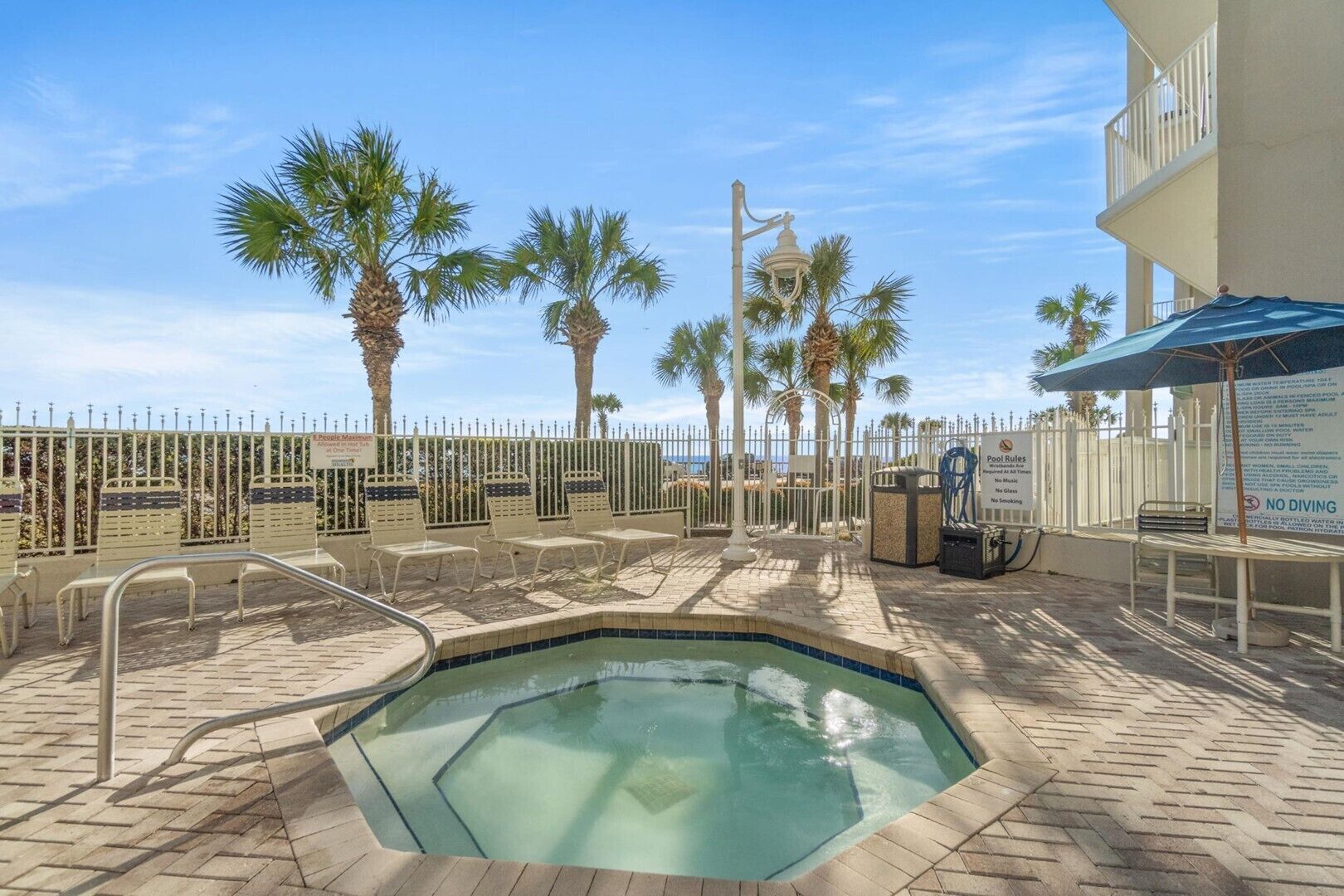 A pool area with lounge chairs, a pool, palm trees, and a fence.