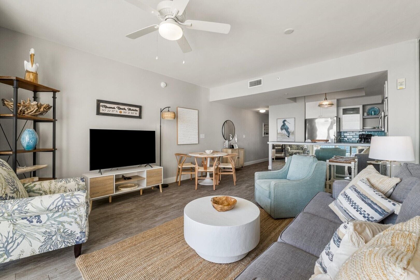 A spacious living room with a flat-screen TV, a dining area, and a kitchen in the background.