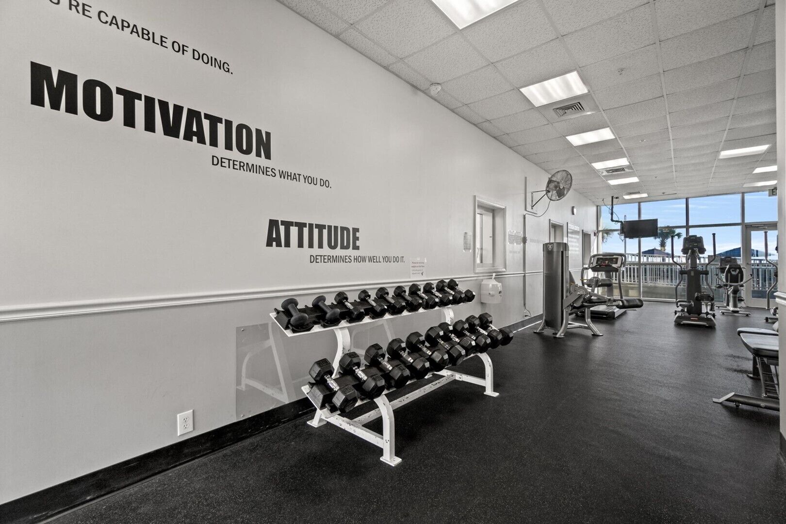 A gym with motivational and attitude posters on the wall, a row of dumbbells, and various exercise equipment.