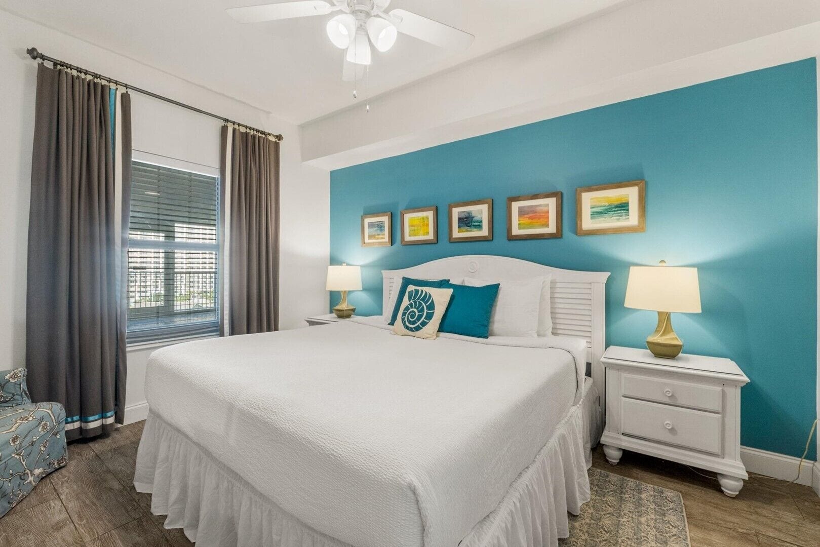 A bedroom with a bed, nightstands, a ceiling fan, a window with curtains, and artwork on the wall.