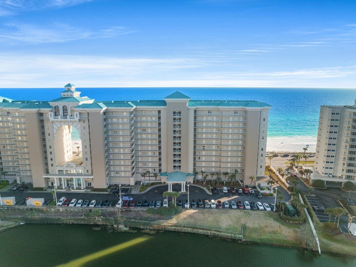 A multi-story hotel with a central atrium, a parking lot, and a view of the ocean.