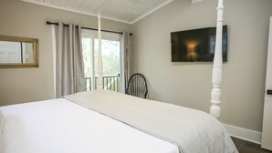 Une chambre avec un grand lit, une chaise, une télévision et un balcon avec des rideaux.