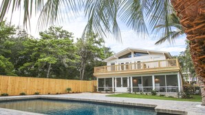 Une maison à deux étages dotée d’une grande terrasse et d’une piscine.