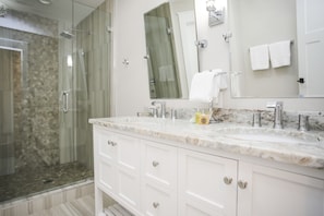Un baño moderno con ducha acristalada, lavamanos de mármol y muebles de color blanco.