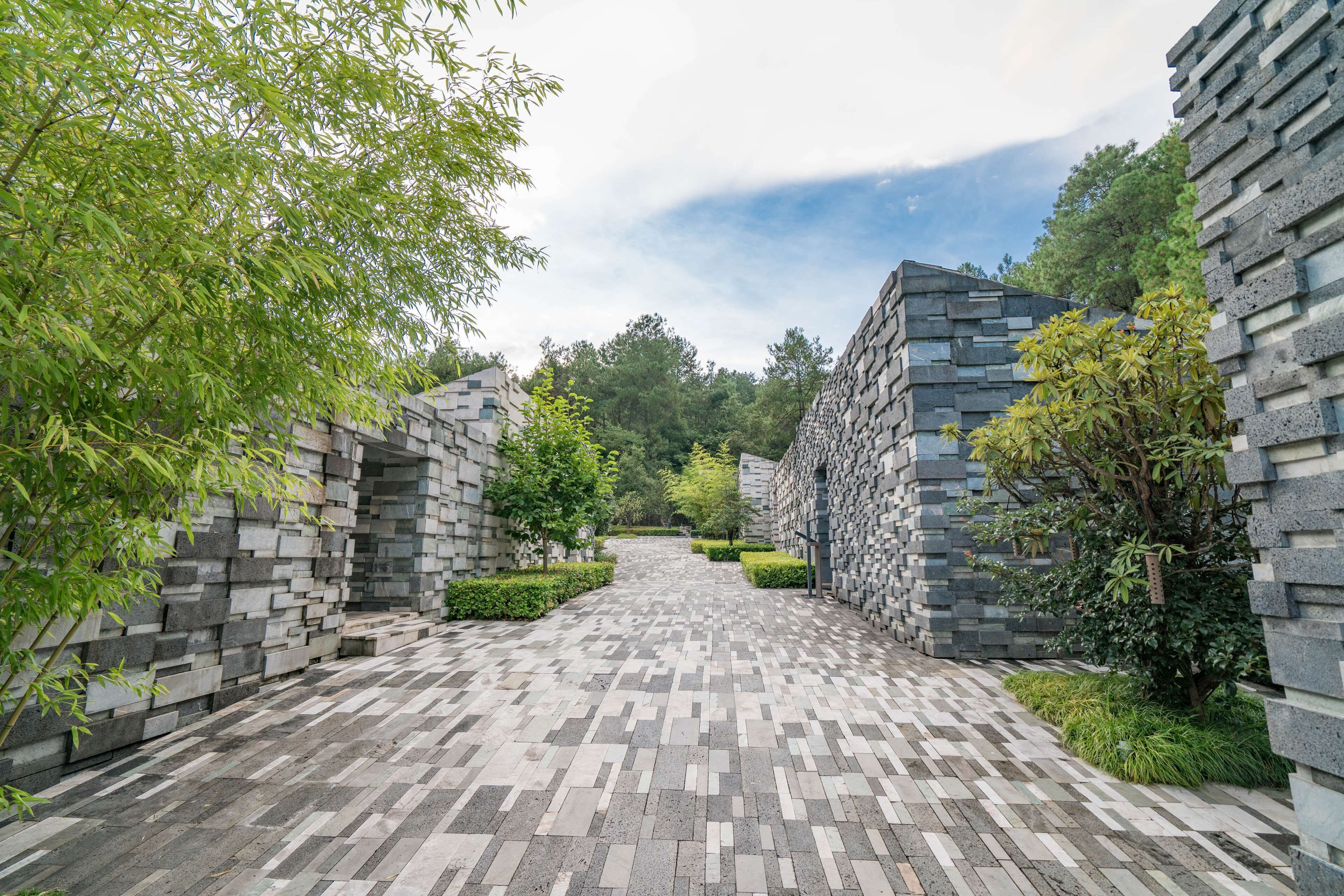 A pathway flanked by stone walls with greenery on both sides.