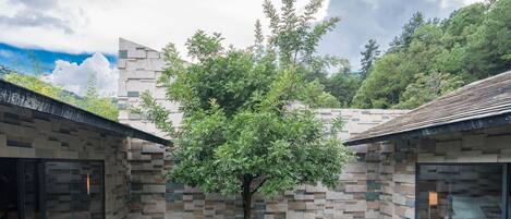 Un edificio moderno con fachada de piedra, dos zonas de estar al aire libre y un árbol en el centro.