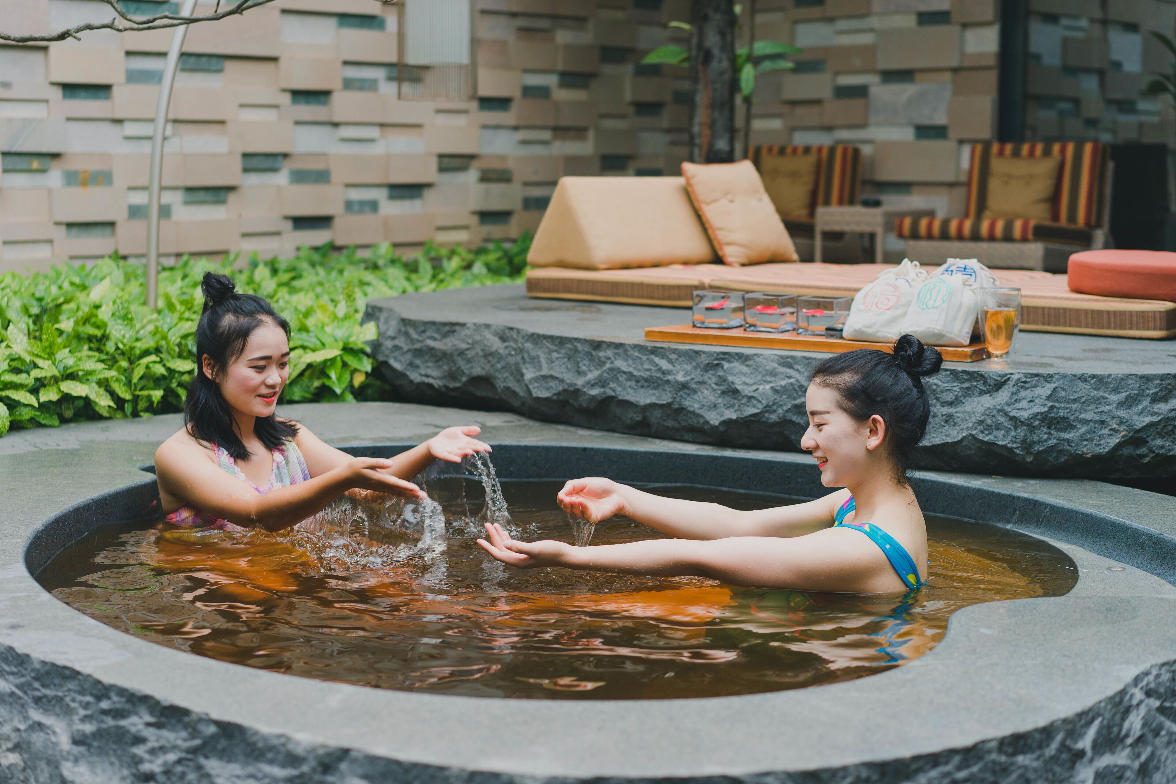 Two people in a hot tub with a stone wall and seating area in the background.