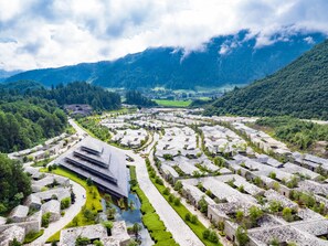 A large, modern complex with multiple buildings arranged in a grid pattern, surrounded by lush greenery and mountains in the background.