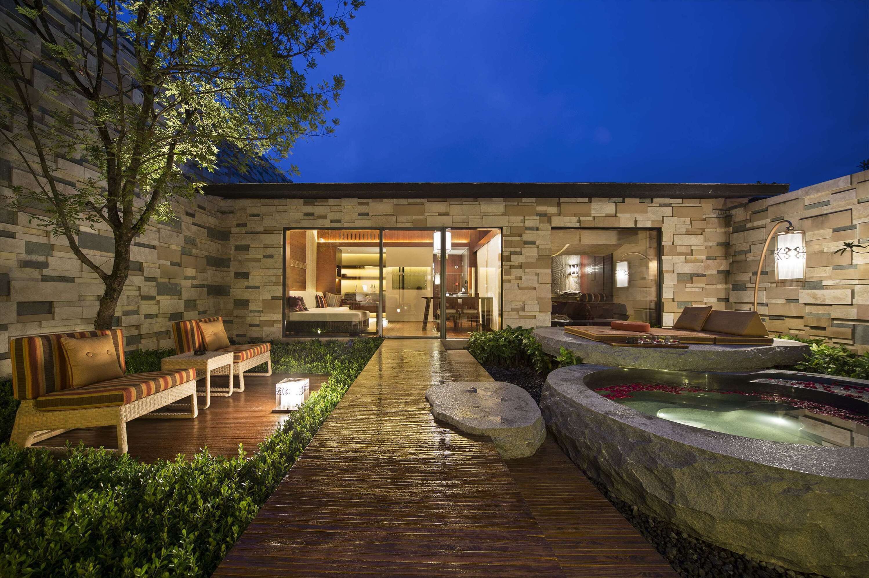 A modern outdoor patio with a stone wall, seating area, and a water feature.