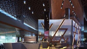 Un moderno vestíbulo de hotel con un diseño geométrico en el techo, una recepción y áreas de estar.