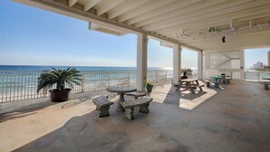 An outdoor patio with stone tables and benches, a view of the ocean, and a white railing. - Fontainebleau Terrace by Panhandle Getaways (Panama City Beach)