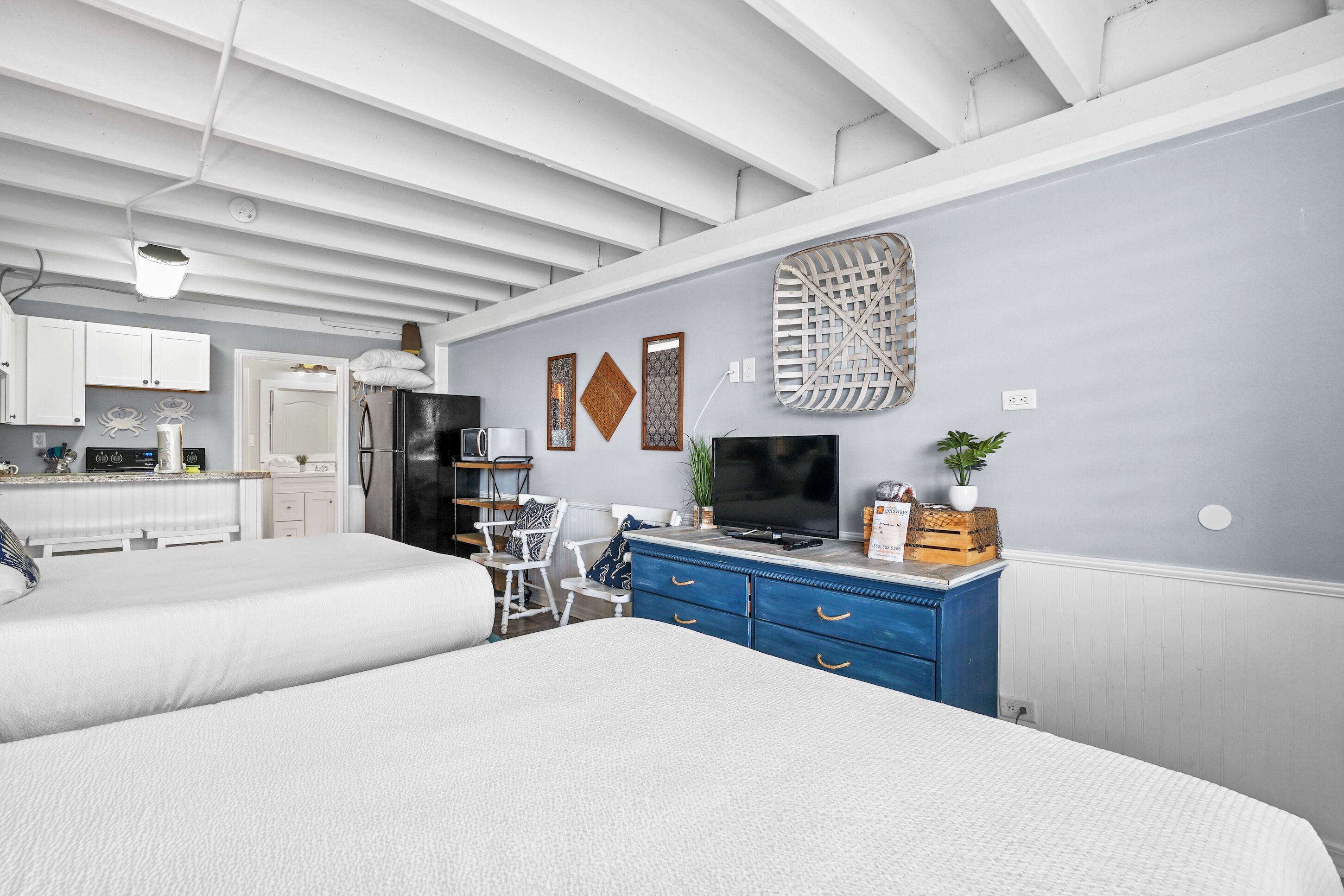 A modern hotel room with a kitchenette, a large bed, a TV, and a blue dresser.
