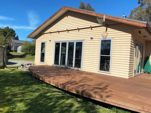 A single-story house with a deck, large sliding glass doors, and a basketball hoop.