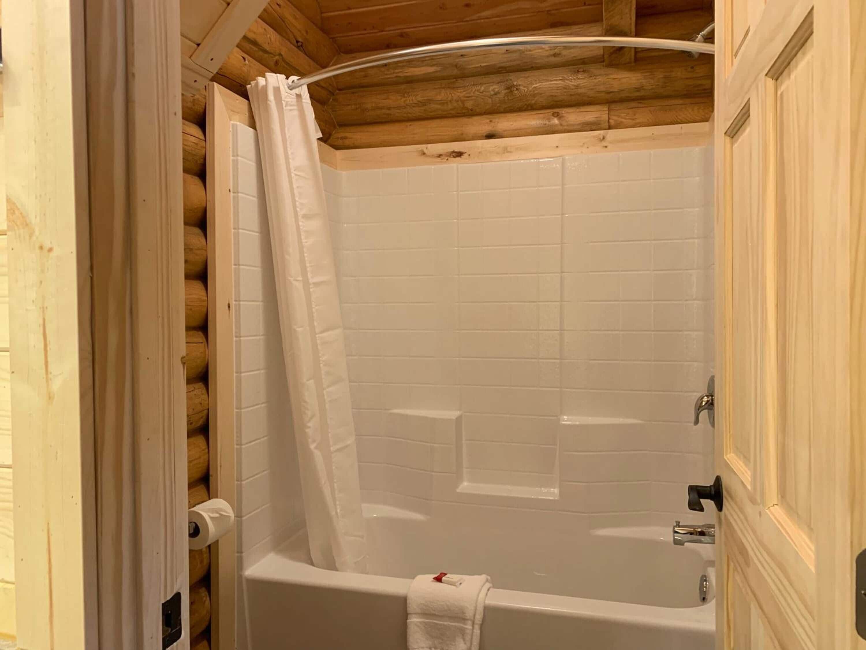 A wooden cabin bathroom with a bathtub, white tiles, and a wooden ceiling.
