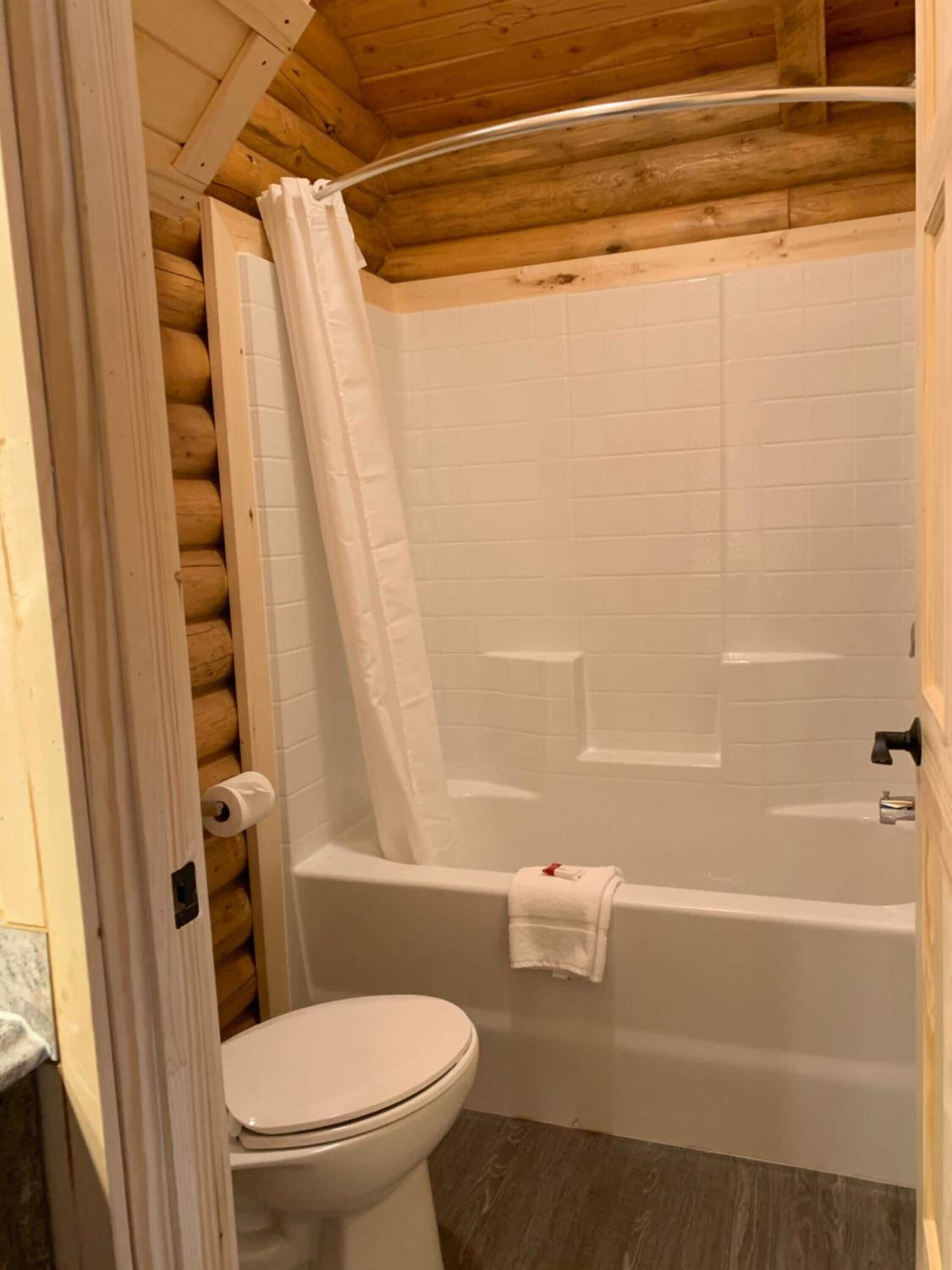 Une salle de bain rustique, aménagée dans une cabane en bois, comprenant des toilettes, une baignoire et un espace douche.