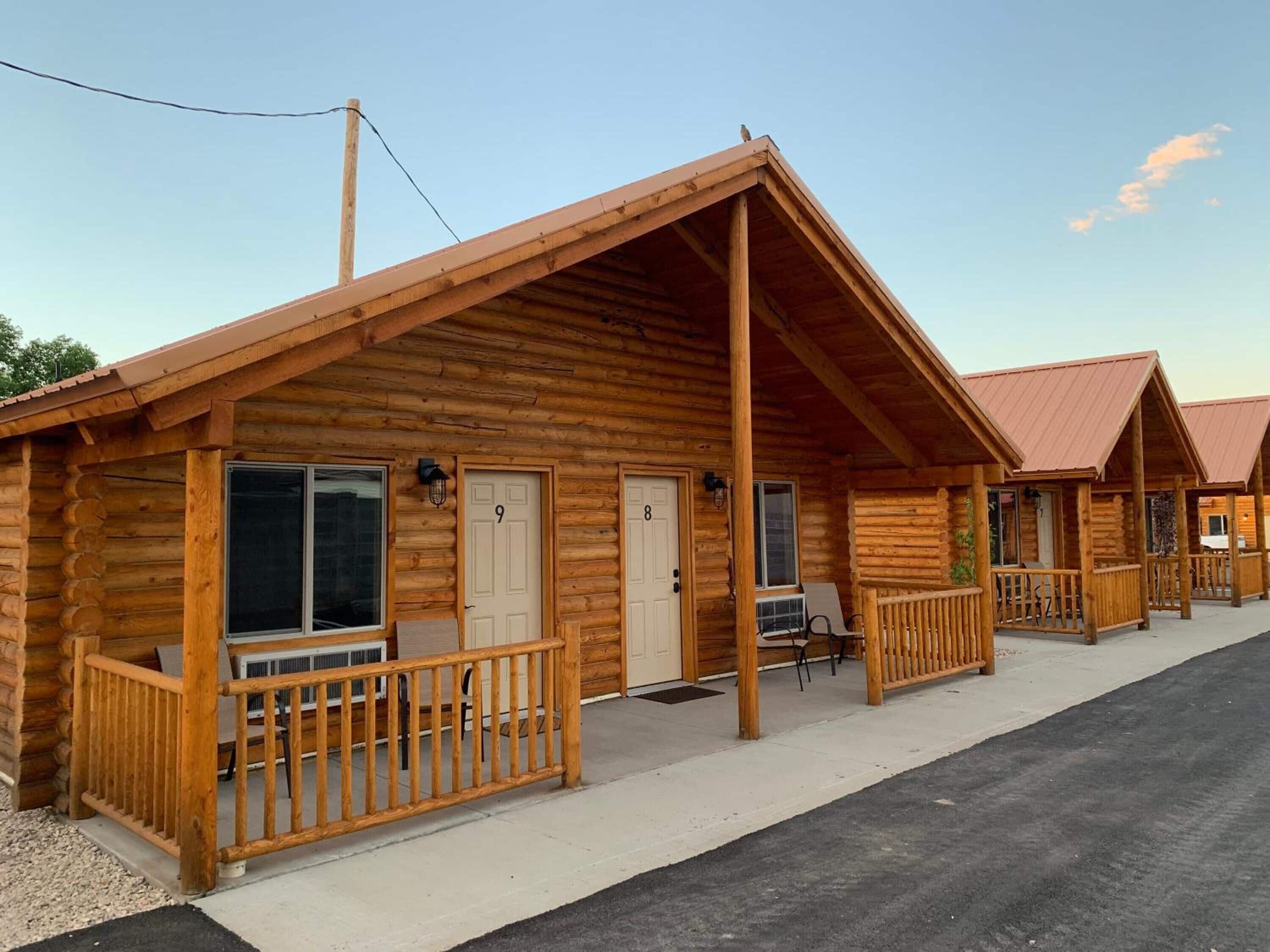 A row of log cabins with wooden exteriors and pitched roofs, each featuring a porch and a door.