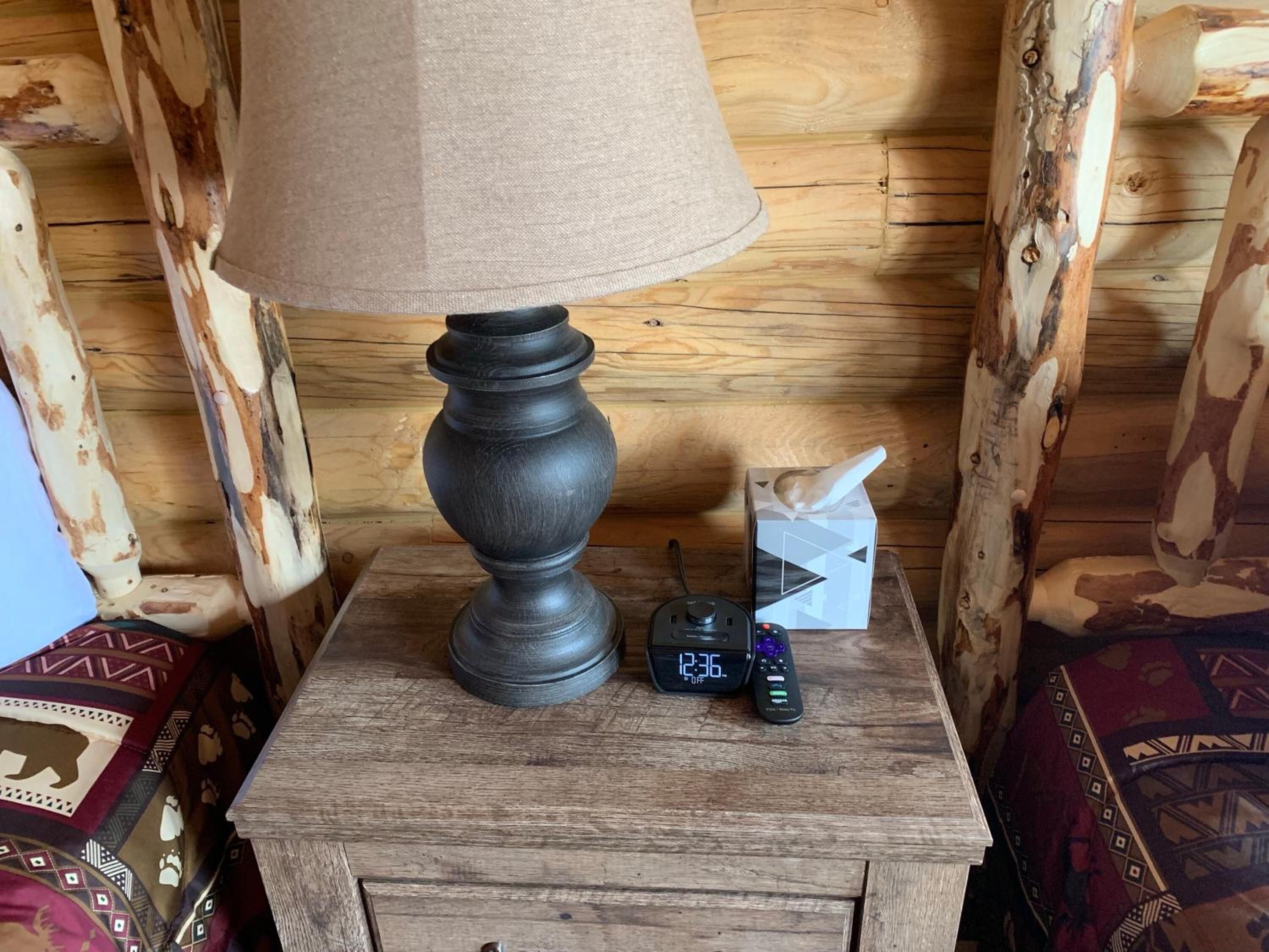 A wooden nightstand with a lamp, a box of tissues, and a remote control.