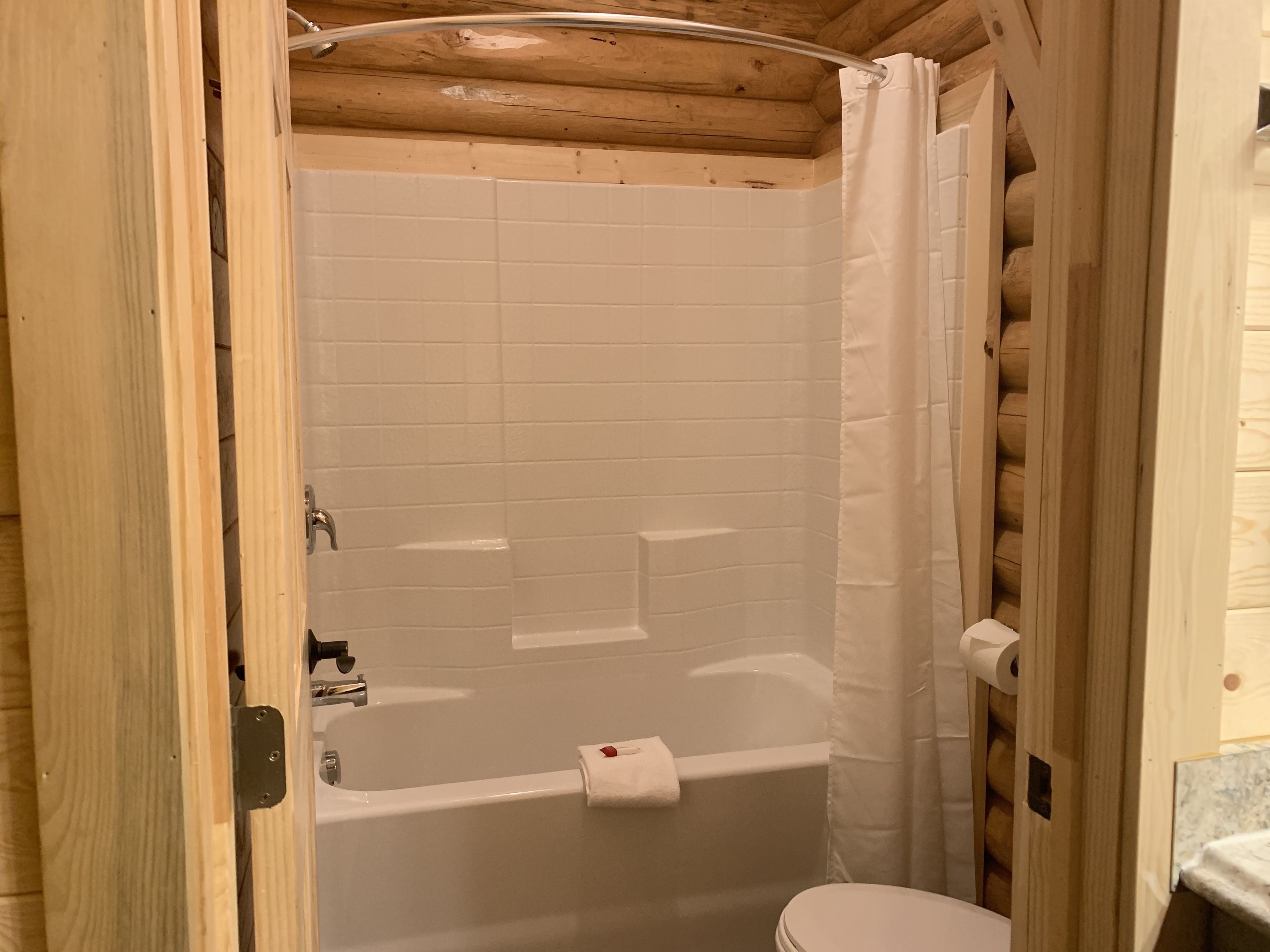 A wooden cabin bathroom with a bathtub, toilet, and shower curtain.