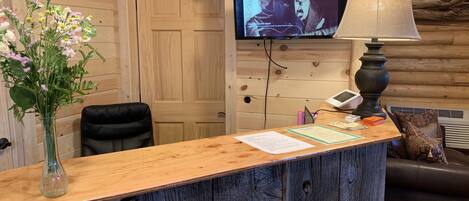 A wooden reception desk with a vase of flowers, a television mounted on the wall, and a lamp.