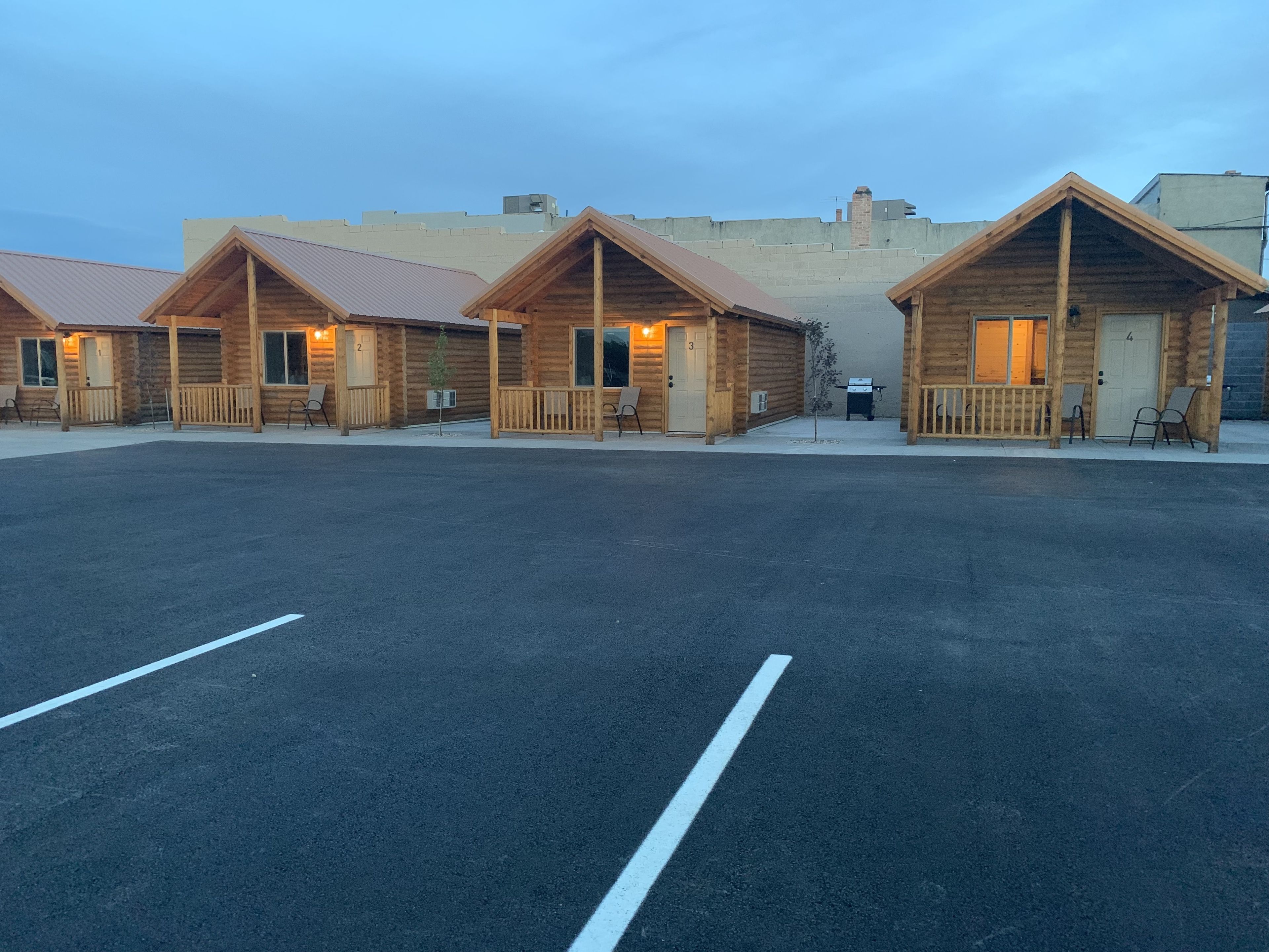 A row of log cabin-style cabins with numbered doors, a paved parking area, and a clear sky.