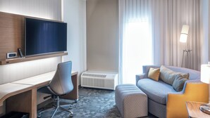 Een hotelkamer met een flatscreen-televisie, een bureau, een comfortabele bank en een staande lamp.