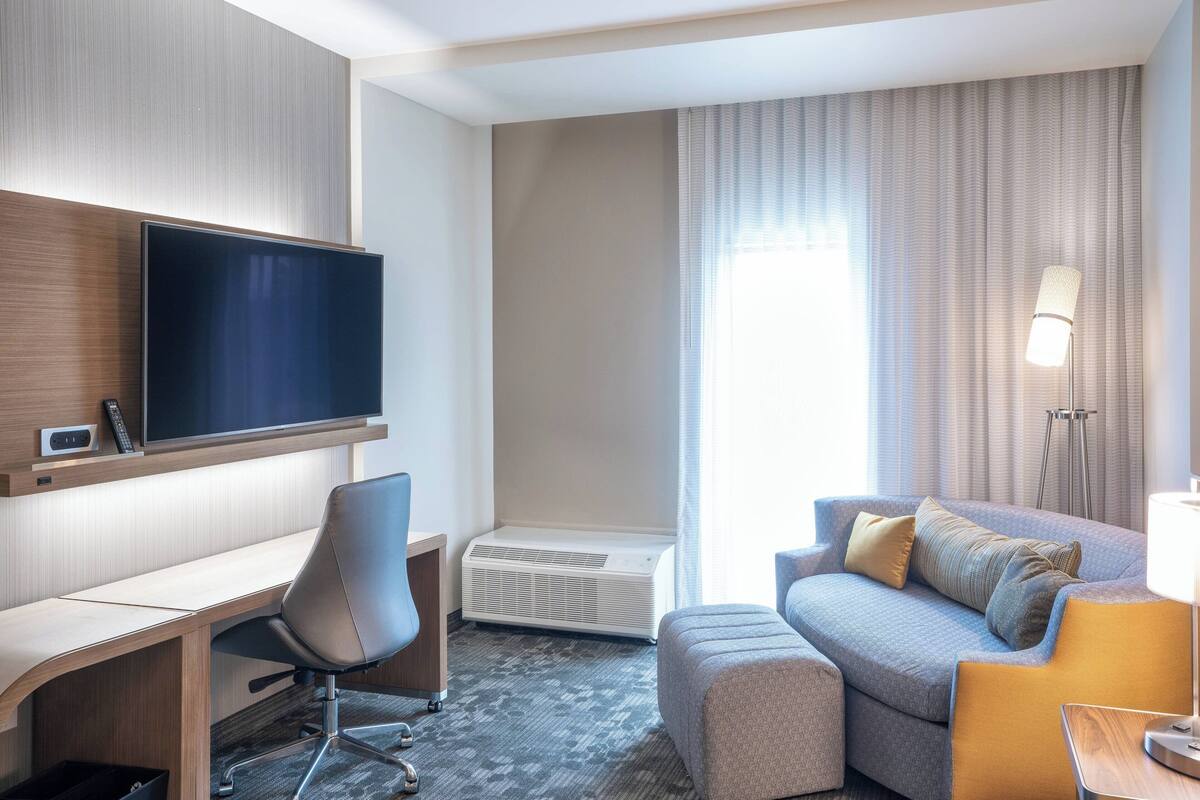 Ein Hotelzimmer mit Flachbildfernseher, Schreibtisch, bequemer Couch und Stehlampe.