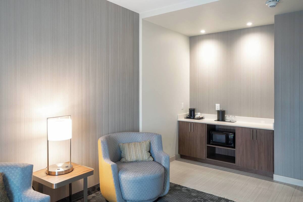Ein modernes Hotelzimmer mit Sitzgelegenheit, einer Lampe, einer Mikrowelle und einer Küchenzeile.