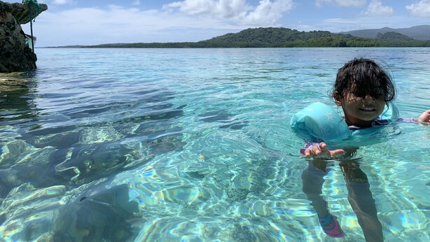 Henkilö kirkkaassa vedessä, taustalla kivikkoinen ranta ja kauempana kukkulat.