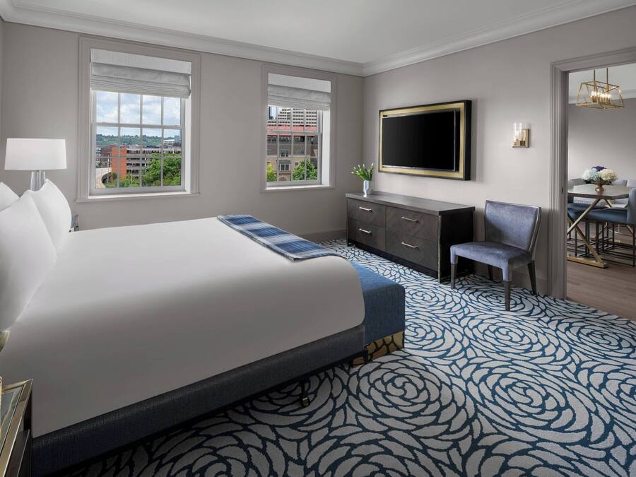 A hotel room with a large bed, a desk, a chair, a TV, and a view of the city.