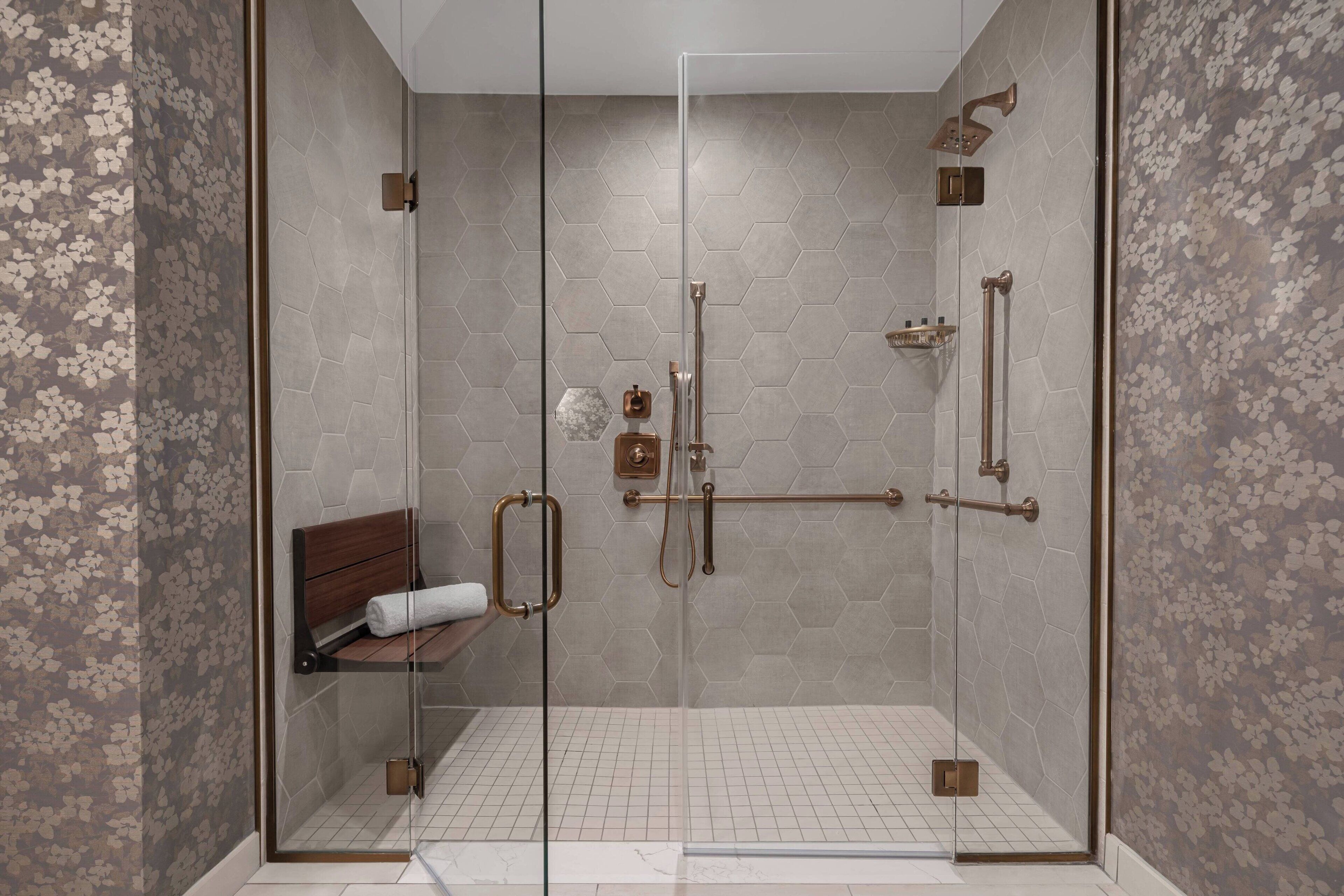 Een douche met glazen wanden, een bankje, een handdoek en een klein plankje.