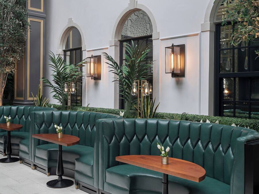 A green leather bench seating area with tables, surrounded by plants and decorative lighting.