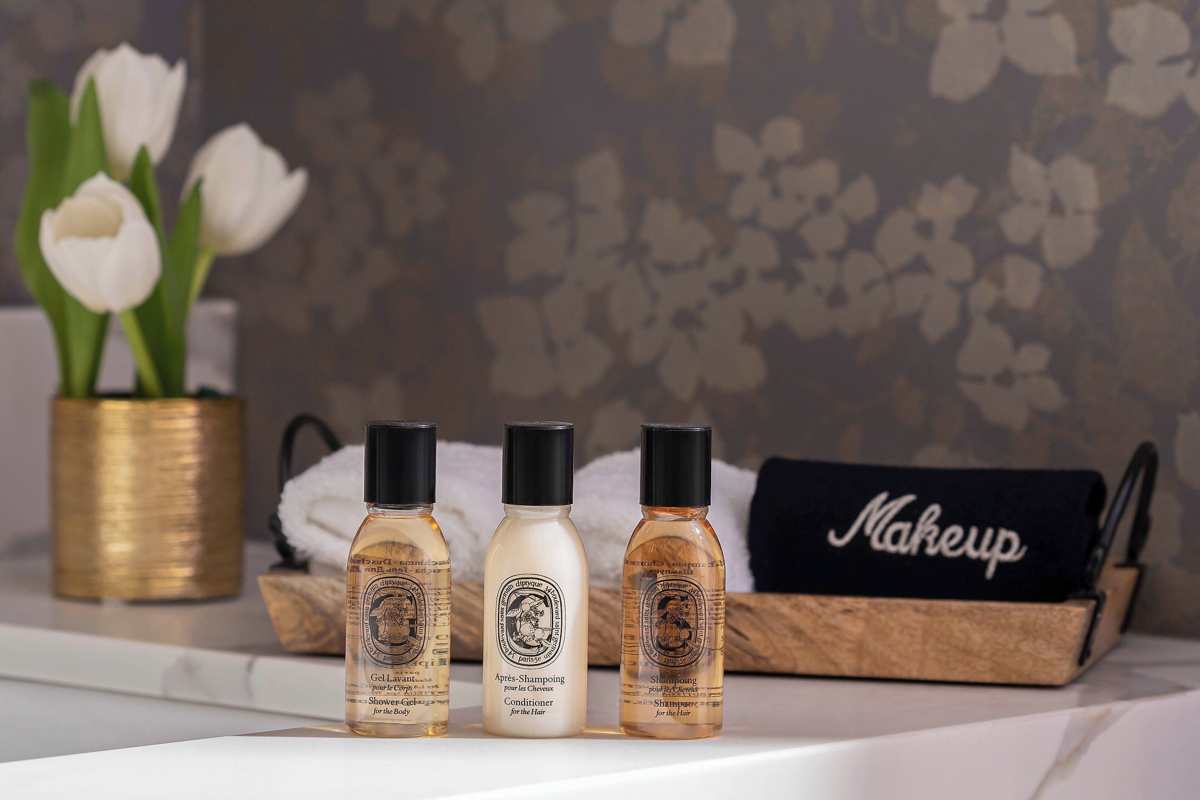 Tres botellas de productos para el cabello sobre una superficie de mármol, un florero dorado con flores blancas y un neceser de maquillaje.