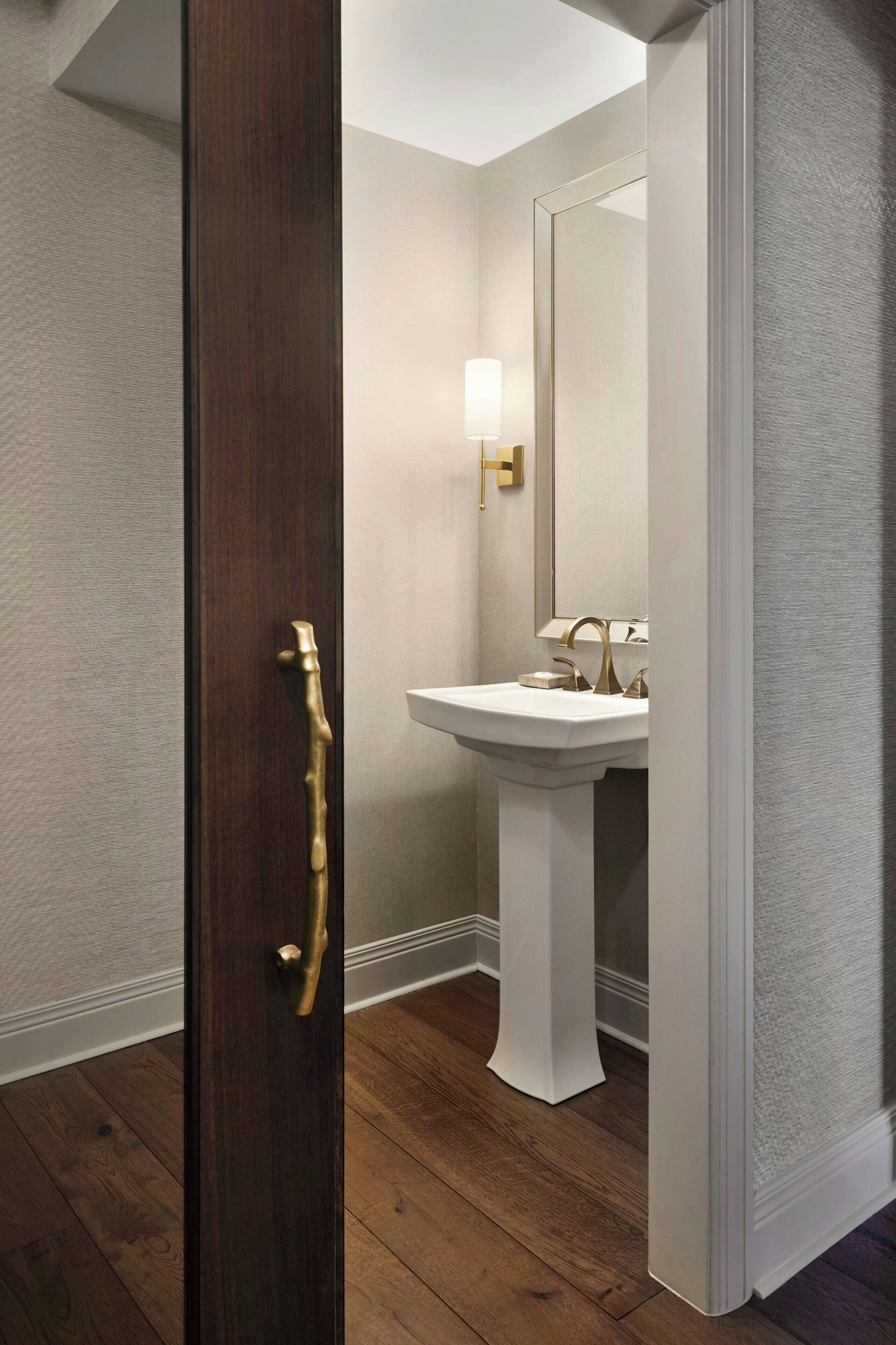 A bathroom with a wooden door, a white pedestal sink, and a wall-mounted light fixture.